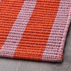 an orange and pink striped rug on top of a wooden floor next to a gray wall