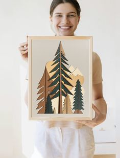 a woman holding up a painting with trees on it