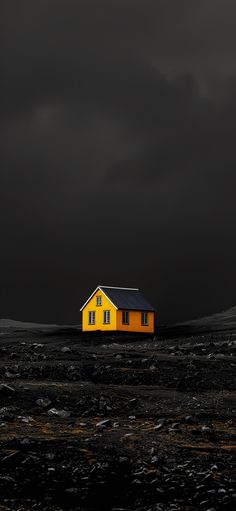 a yellow house sitting on top of a black field under a dark sky with clouds