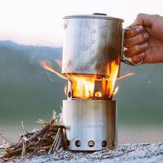 a person holding a coffee pot over a campfire with flames coming out of it