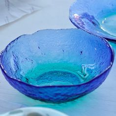 two blue glass bowls sitting on top of a white table next to plates and utensils