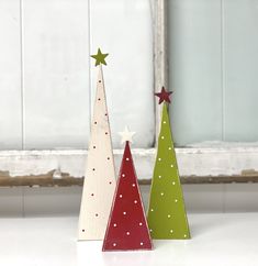 three wooden christmas trees sitting on top of a white table next to a window sill