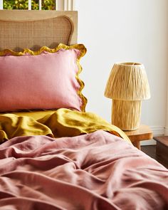 a bed with pink and yellow sheets in front of a lamp on a wooden table