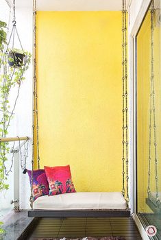 a swing bed in front of a yellow wall with plants growing on it and hanging from the ceiling