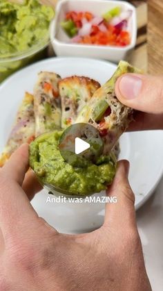 a person holding a piece of pizza on top of a white plate with guacamole