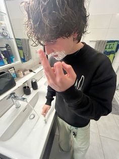 a young man standing in front of a bathroom sink making the peace sign with his hand