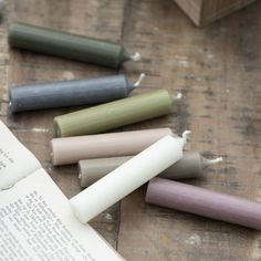 some candles are laying next to an open book on a wooden table with writing paper