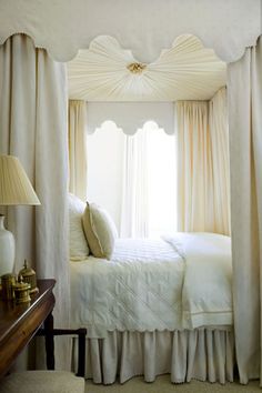 a white bed sitting in a bedroom next to a window with drapes on it