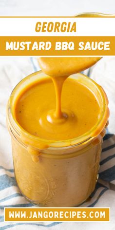 a jar filled with mustard sauce on top of a striped table cloth next to a spoon