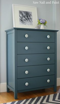 a blue dresser with white knobs and drawers in the corner, next to a striped rug