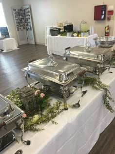 there are many silver trays on the table with flowers and greenery around them