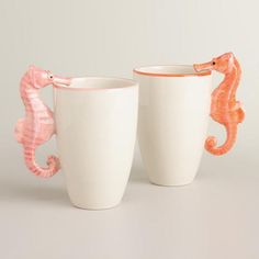 two white cups with seahorses on the side and one is holding a cup