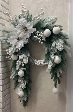 a christmas wreath hanging on the wall next to a brick fireplace with white balls and greenery