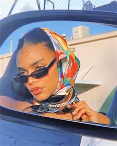 a woman wearing sunglasses and a scarf is looking in the rear view mirror