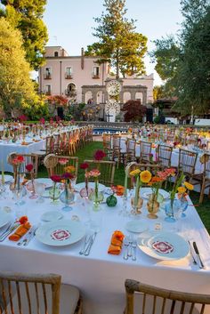 a table set up with plates and flowers for an outdoor wedding reception in front of a large building