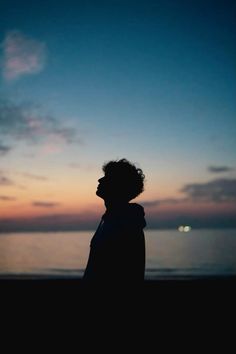 a man standing on top of a beach next to the ocean at sunset or dawn