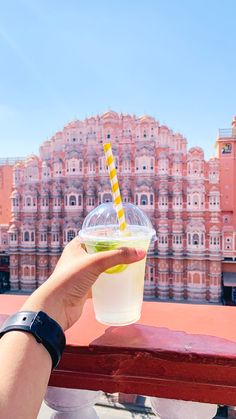 a person holding up a plastic cup with a yellow and green straw in front of a pink building