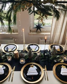 the table is set with black and gold place settings, pine cones, evergreen leaves, candlesticks, and white napkins