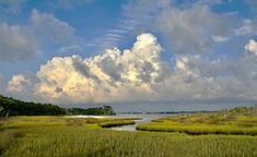 the sky is filled with clouds and green grass in front of a body of water