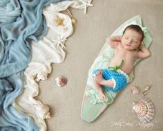 a baby laying on top of a surfboard next to seashells and starfish