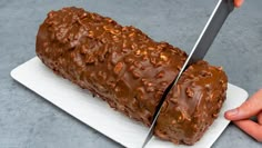 a person cutting into a chocolate cake on top of a white plate with a knife