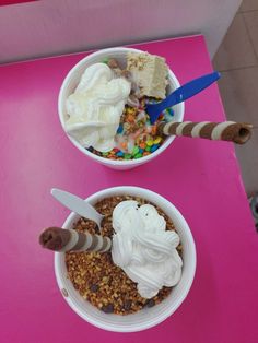 two bowls filled with ice cream and granola on top of a pink countertop