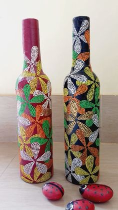 two painted wine bottles sitting next to each other on a wooden floor with ladybugs