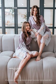 two women sitting on a couch in matching robes and posing for the camera with their legs crossed