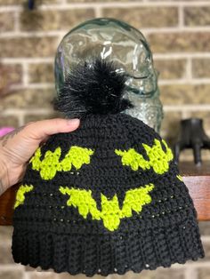 a knitted batman hat with yellow and black bats on it, being held up by someone's hand