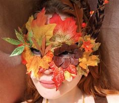 a woman with leaves on her face is wearing a leafy headdress and feathers