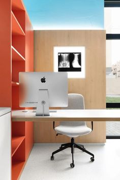 an apple computer sitting on top of a white desk in front of a book shelf