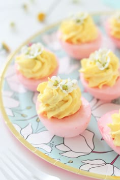 small pink and yellow desserts with white flowers on them sitting on a blue plate