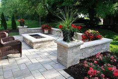 a brick patio with chairs and fire pit surrounded by flowers in the back yard area