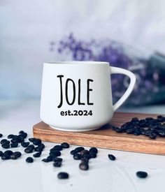 a white coffee mug sitting on top of a wooden cutting board next to black beans