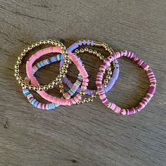 three bracelets are sitting on top of a wooden table and one is purple, the other is pink