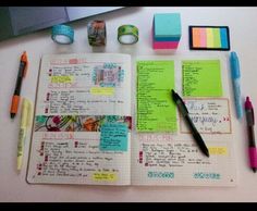 an open notebook sitting on top of a table next to some pens and sticky notes