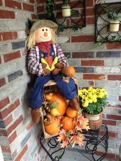 a scarecrow sitting on top of a pile of pumpkins next to some flowers