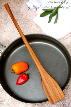 two peppers and a wooden spatula sitting on top of a frying pan next to utensils