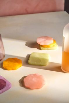 several different colored cookies next to a bottle of liquid on a white counter with pink and yellow accents