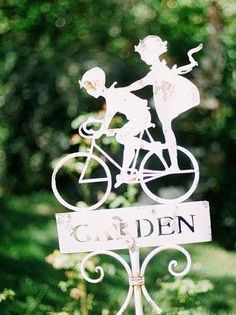 a white sign that says garden with a man and woman riding a bike on it