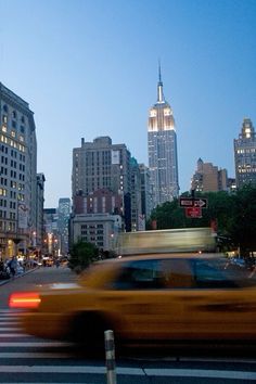 a yellow taxi driving down a street next to tall buildings in the city at night