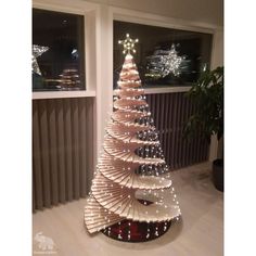 a christmas tree made out of strips of cardboard with lights on it in front of a window