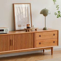 a wooden cabinet with drawers and a clock on it next to a plant in a living room