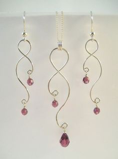 three silver necklaces with pink crystal beads hanging from it's sides on a white surface