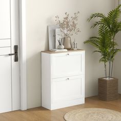 a white cabinet sitting next to a potted plant on top of a wooden floor