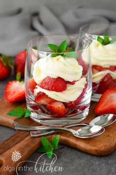 two desserts with strawberries and whipped cream in them on a wooden cutting board