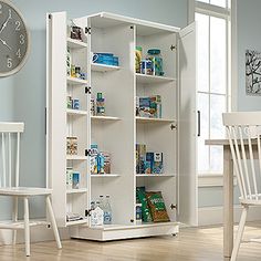 a white pantry with lots of food and drinks on it's shelves next to a clock