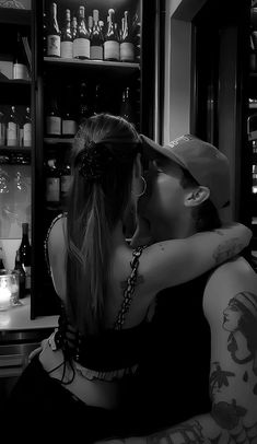 two people are kissing in front of an open refrigerator with many bottles on the shelves