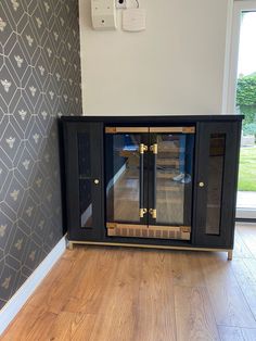 a black cabinet with glass doors in a room next to a wallpapered wall