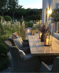 a wooden table surrounded by wicker chairs with candles on it in front of a house